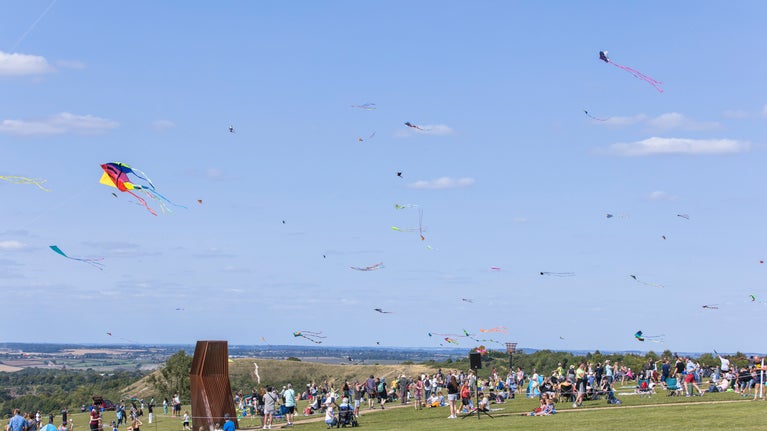 looking towards the windcatcher, the grass at the Downs is full of people picnicking and flying kites. The blue sky is full of colourful kites.